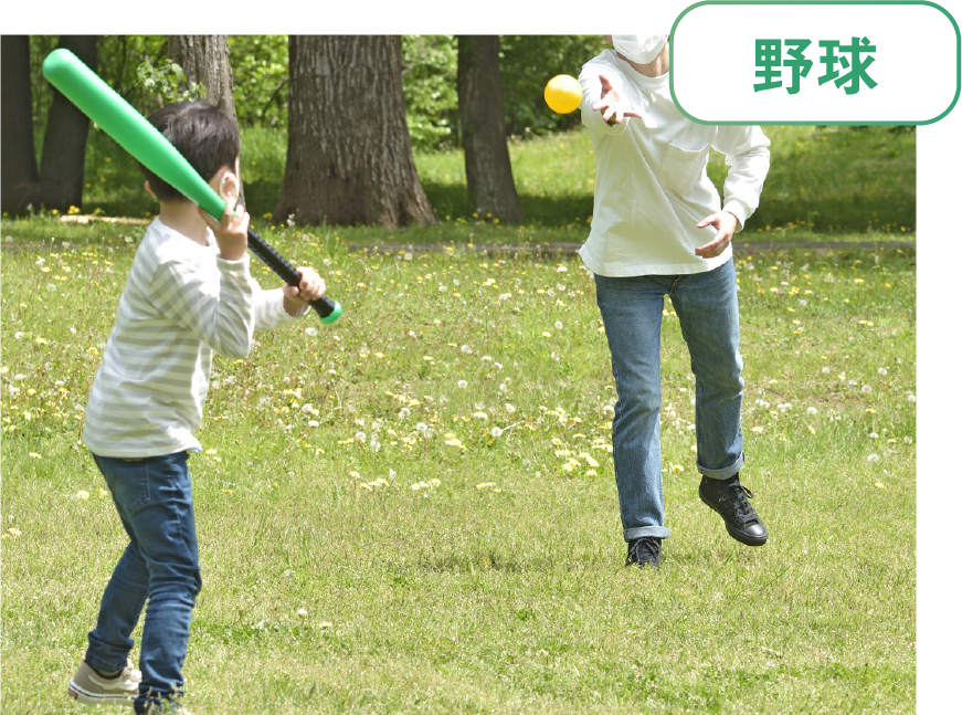 「野球」大人がボールを投げて子供がバットで打とうとしている写真